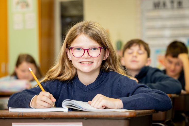 Young girl in a colorful classroom, smiling enthusiastically while learning at her school desk.