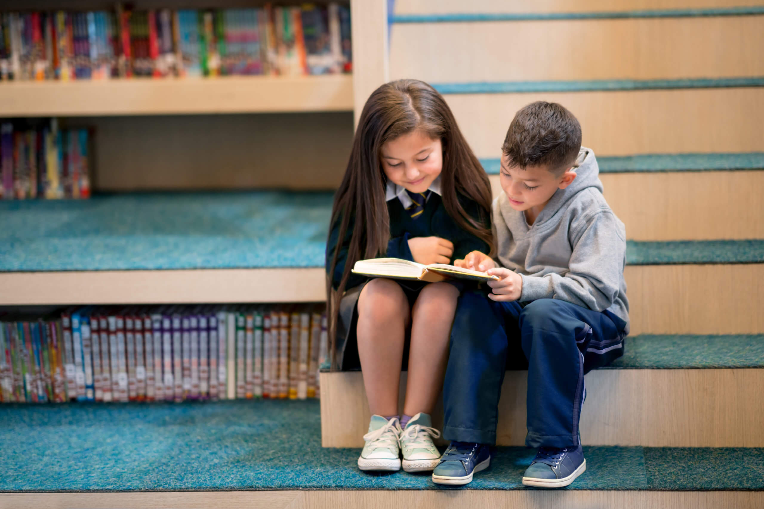 2 young students reading a book together on the library stairs