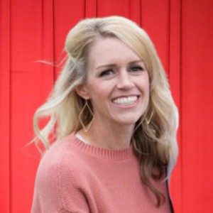 Smiling woman with blonde hair in a pink sweater against a vibrant red background.