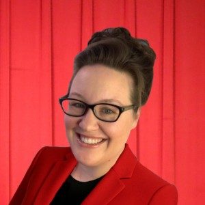 Cheerful woman in red blazer smiles confidently against a vibrant backdrop.